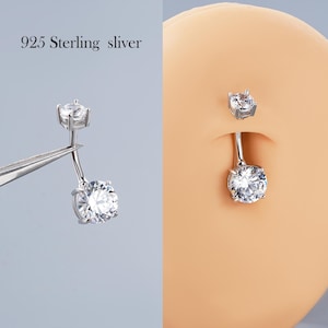 Puede incluir: Un piercing de ombligo plateado con una gema redonda y transparente grande. El anillo se sujeta con pinzas a la izquierda y lo lleva una persona a la derecha. El texto "925 Sterling sliver" está en la esquina superior izquierda.