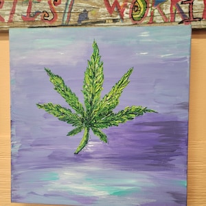 Könnte beinhalten: Ein quadratisches Leinwandgemälde mit einem strukturierten, leuchtend grünen Cannabisblatt, das vor einem Hintergrund aus violetten, lavendelfarbenen und hellblauen Pinselstrichen zentriert ist. Das Blatt zeigt detaillierte, erhabene Farbaufträge.