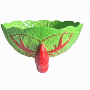 May include: A bright green ceramic bowl with a scalloped rim and a textured surface resembling cabbage leaves. The exterior features a red crawfish motif, and the bowl is supported by a single, prominent red crawfish-shaped base.