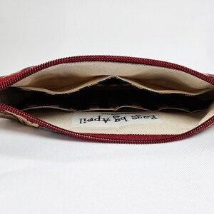 May include: Open view of a fabric pencil case with a red zipper. The interior has multiple pockets. The exterior fabric has a pattern of navy, tan, and red. The text "Bags by April" is visible inside the case.