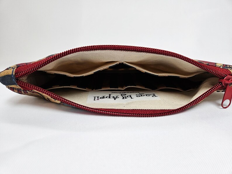 May include: Open view of a fabric pencil case with a red zipper. The interior has multiple pockets. The exterior fabric has a pattern of navy, tan, and red. The text "Bags by April" is visible inside the case.