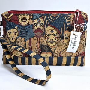 May include: A rectangular clutch with a zipper closure and a wrist strap. The clutch features a print of vintage circus clowns in shades of red, blue, and tan. The wrist strap has a navy blue and tan striped pattern. A tag reads "Bags by Appell".