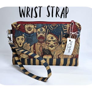 May include: A rectangular wrist strap bag with a zipper closure and a wrist strap. The bag features a print of vintage clowns in various expressions. The wrist strap is black and gold striped. The text "WRIST STRAP" is above the bag.