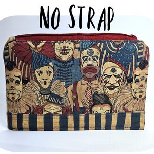 May include: A rectangular zippered pouch featuring a collage of vintage-style clown faces in various expressions. The pouch has a red zipper and a striped bottom. The text "NO STRAP" is printed at the top.