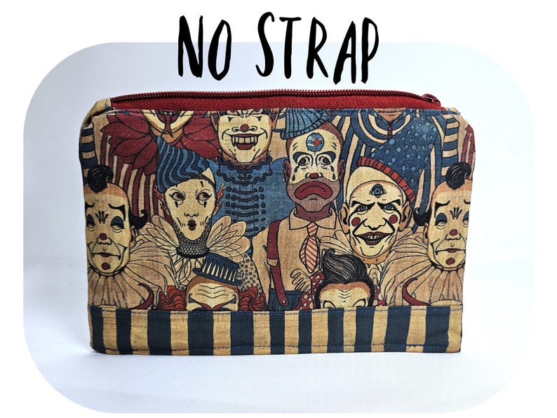 May include: A rectangular zippered pouch featuring a collage of vintage-style clown faces in various expressions. The pouch has a red zipper and a striped bottom. The text "NO STRAP" is printed at the top.