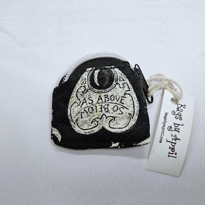 May include: A small black coin pouch featuring a white ouija board planchette graphic with the text AS ABOVE SO BELOW. The pouch has a white zipper closure and a white paper tag attached with string that reads Bags by April and bagsbyapril.com.