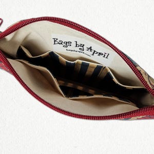 May include: Open red zippered pouch with a floral pattern. The interior features multiple pockets and a label that reads "Bags by April". The lining is beige, and the pockets have a striped design.