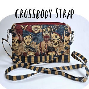 May include: Crossbody strap bag featuring a colorful illustration of vintage circus clowns. The bag has a black and tan striped strap and a red zipper. The text "CROSSBODY STRAP" is printed on the top of the bag.