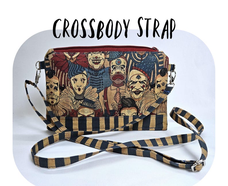 May include: Crossbody strap bag featuring a colorful illustration of vintage circus clowns. The bag has a black and tan striped strap and a red zipper. The text "CROSSBODY STRAP" is printed on the top of the bag.