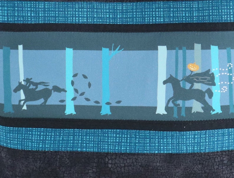 May include: A fabric panel featuring a Halloween-themed design. The artwork depicts a headless horseman riding a horse through a forest. The color palette includes shades of blue, teal, and black, creating a spooky atmosphere. The design is bordered by textured stripes.