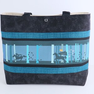 May include: A large tote bag with a black textured exterior and teal accents. The central panel features a forest scene with silhouetted figures on horseback. The bag has two black handles and a beige interior.