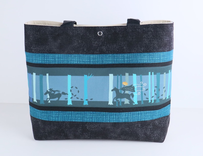 May include: A large tote bag with a black textured exterior and teal accents. The central panel features a forest scene with silhouetted figures on horseback. The bag has two black handles and a beige interior.