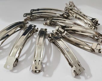 May include: A collection of shiny, silver-colored metal hair barrettes. The barrettes are curved and have a hinged clasp mechanism. They are arranged on a white surface, reflecting light.
