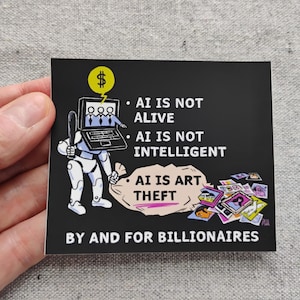 Op de afbeelding: Een zwarte vierkante sticker met witte tekst en een cartoonillustratie. De illustratie toont een robot met een laptop en een geldbuidel. De tekst luidt: "AI IS NOT ALIVE, AI IS NOT INTELLIGENT, AI IS ART THEFT BY AND FOR BILLIONAIRES."