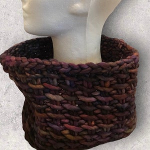 May include: A thick, chunky knit cowl in shades of brown, purple, and pink. The cowl is made with a textured stitch and has a wide, open design.