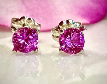 May include: A pair of silver stud earrings with a round, faceted, purple gemstone in each.