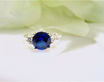 May include: A silver ring with a large, round, dark blue gemstone surrounded by smaller, clear gemstones.