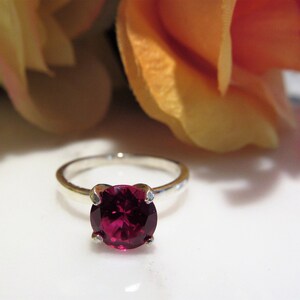 May include: A silver ring with a large, round, deep red gemstone.
