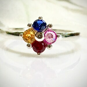 May include: A silver ring featuring a cluster of four colourful gemstones. The stones are blue, yellow, red and pink.