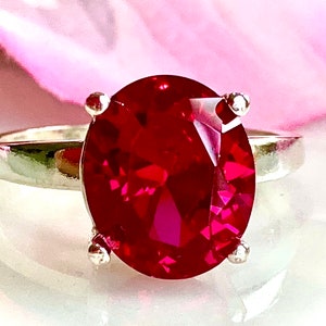 May include: A silver ring with a large, oval-shaped, deep red gemstone.