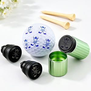 May include: A golf gift set with a white golf ball printed with blue designs and the name "JAY", two wooden golf tees, and a green metal container with two black stampers. The stampers have the text "YAL".
