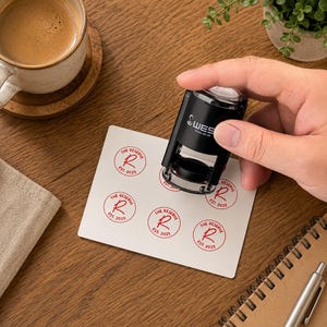 May include: A black self-inking stamp with the text WES Printer SC-20, used to create red circular impressions on a white card. Each circular stamp design features the text THE RESERVE, a large letter R, and the year EST. 2025 in red ink.