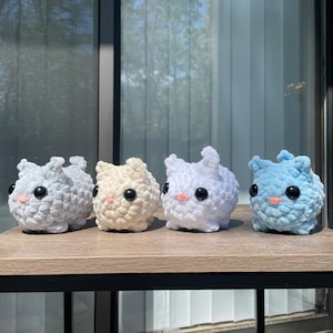May include: Four crocheted plush toys in different colors: light gray, cream, white, and light blue. Each toy has a round body, two small ears, and black button eyes.