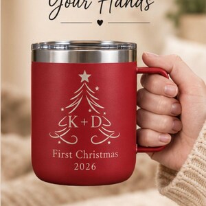 May include: A red insulated mug with a silver rim and handle, featuring a white engraved Christmas tree graphic with the text K + D, First Christmas 2026. The image includes the text Comfort in Your Hands and Perfect for Home, Office or on the Go.