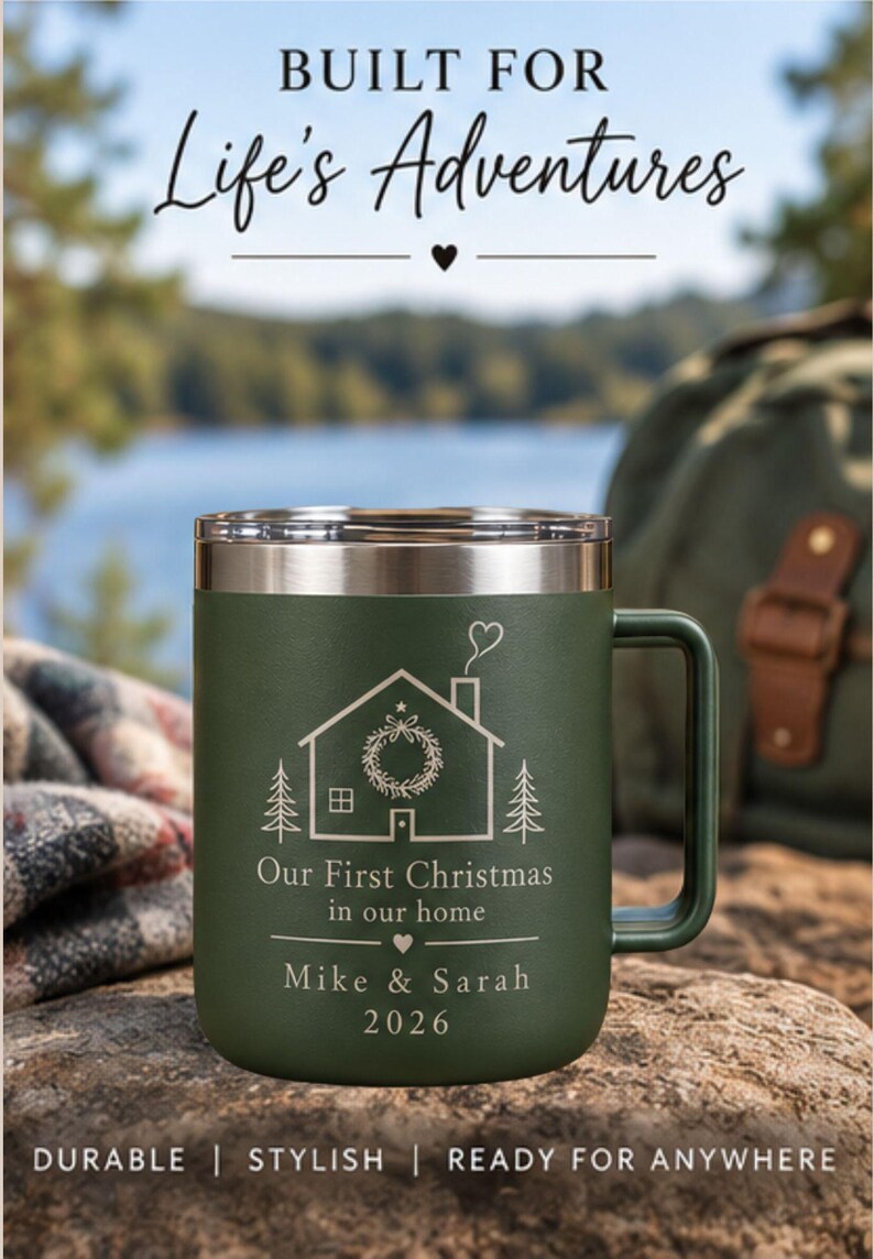 May include: A matte olive green stainless steel mug with a silver rim and handle. The mug features an engraved design of a house with a wreath, pine trees, and the text "Our First Christmas in our home", "Mike & Sarah", and the year "2026".