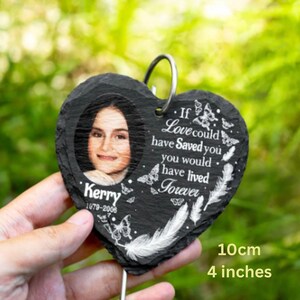 Puede incluir: Memorial de pizarra negra en forma de coraz&oacute;n con una foto de una mujer y el texto "Kerry 1979-2006". La pizarra tambi&eacute;n tiene el texto "Si el amor te hubiera salvado, habr&iacute;as vivido para siempre" con un dise&ntilde;o de pluma blanca y mariposa. La pizarra tiene un di&aacute;metro de 10 cm.