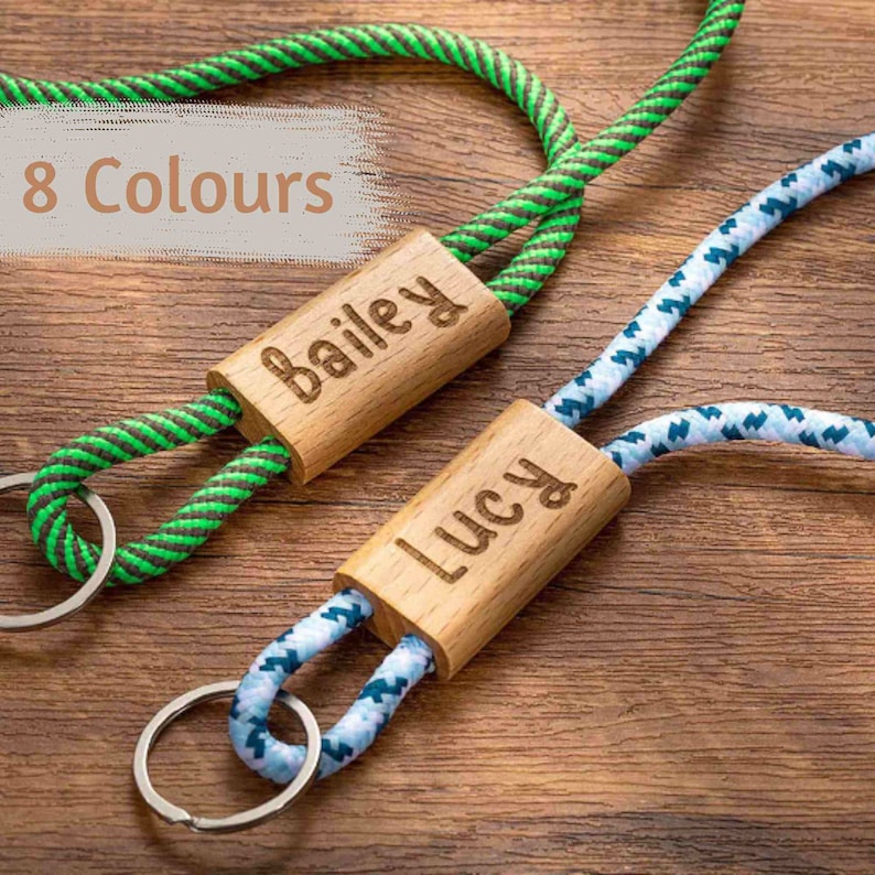 Pode incluir: Dois chaveiros de madeira personalizados com cord&otilde;es de corda. O chaveiro &agrave; esquerda tem um cord&atilde;o listrado verde e marrom e diz "Bailey". O chaveiro &agrave; direita tem um cord&atilde;o listrado azul e branco e diz "Lucy".