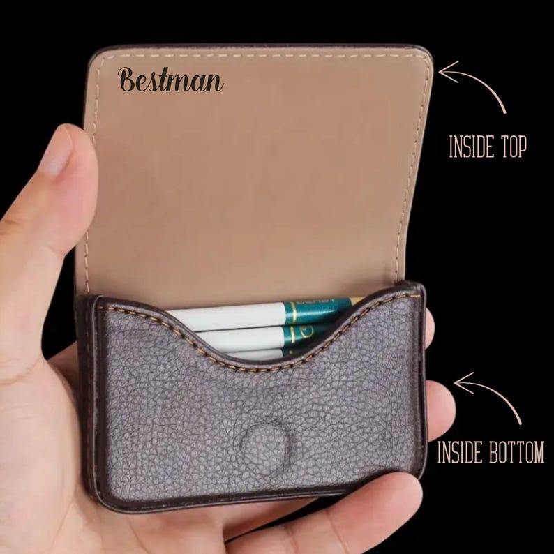 May include: A brown leather cigarette case with a tan interior, held open to reveal cigarettes. The case has the word "Bestman" printed on the inside top.
