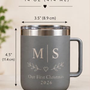 May include: A gray stainless steel mug with a handle and lid, featuring the text THE PERFECT SIZE, 14 OZ (414 ML), M | S, a heart, leaf sprigs, Our First Christmas, and 2026. Dimensions are 3.5 inches wide, 4.5 inches high, and 4.75 inches wide total.
