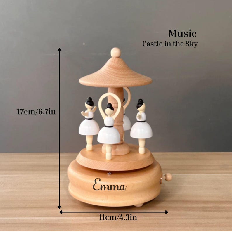 Puede incluir: Una caja de m&uacute;sica de carrusel de madera con cuatro figuras de bailarinas con vestidos blancos. La caja de m&uacute;sica mide 17 cm de alto y 11 cm de ancho, con el nombre "Emma" en la base. Tambi&eacute;n se ve el texto "Music Castle in the Sky".