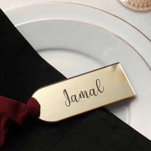 Clear acrylic place card with elegant font positioned on a wedding reception table, with candles and soft lighting, showcasing its versatility as a guest gift, seating name tag, or proposal box accent.