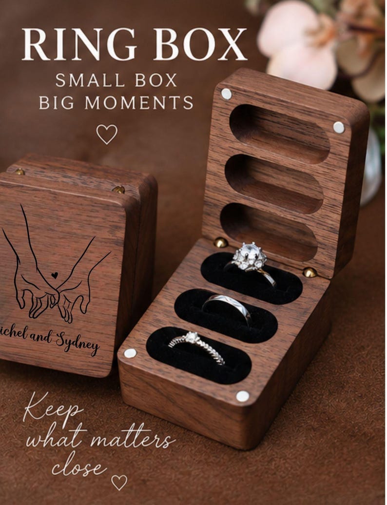 May include: A rectangular dark wood ring box with a hinged lid, featuring a laser-engraved illustration of two hands holding each other and the text 'ichel and Sydney'. The interior has three black velvet slots holding three silver rings.