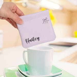 May include: A lavender fabric pouch with a small black cherry design and the name "Hailey" printed in black cursive lettering.
