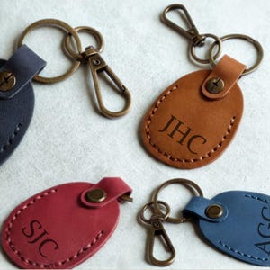 Pu&ograve; includere: Una collezione di portachiavi personalizzati in pelle in vari colori: marrone, blu navy, rosso e blu. Ogni portachiavi presenta iniziali e un moschettone e anello in metallo. I portachiavi sono di forma ovale con bordi cuciti.