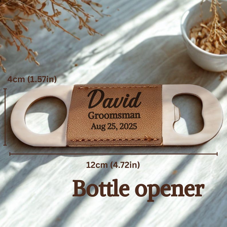 May include: A bottle opener with a tan leather center section engraved with "David, Groomsman, Aug 25, 2025." The opener is 12cm long and 4cm wide. The words "Bottle opener" are at the bottom.