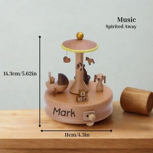 Puede incluir: Una caja de m&uacute;sica de carrusel de madera en color marr&oacute;n claro. Presenta peque&ntilde;as figuras de animales, como un perro, un caballo y un pato. El texto "Mark" est&aacute; en la base. Las dimensiones son 11 cm de ancho y 14,3 cm de alto.