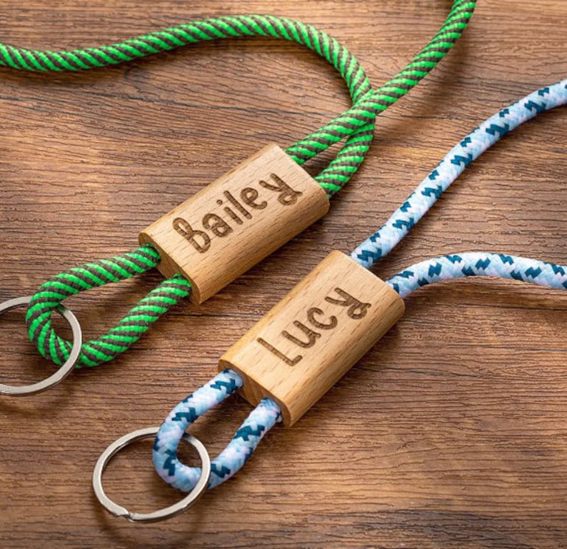 Pode incluir: Dois chaveiros de madeira personalizados com cord&otilde;es de corda. O chaveiro &agrave; esquerda tem um cord&atilde;o de corda verde e preto e diz "Bailey" na etiqueta de madeira. O chaveiro &agrave; direita tem um cord&atilde;o de corda azul e branco e diz "Lucy" na etiqueta de madeira.