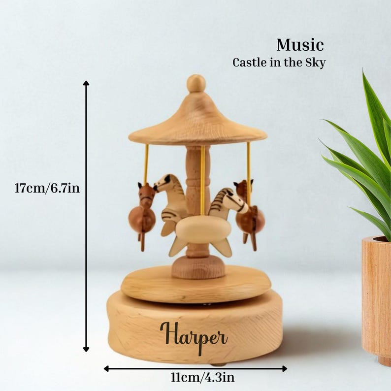Puede incluir: Una caja de m&uacute;sica de carrusel de madera con cuatro figuras de caballos. La caja de m&uacute;sica mide 17 cm de alto y 11 cm de ancho. El texto "Music Castle in the Sky" est&aacute; encima del carrusel. El nombre "Harper" est&aacute; grabado en la base.