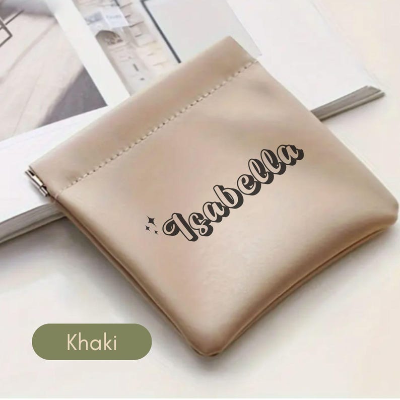 May include: A beige drawstring pouch with the name "Isabella" printed in black. The pouch is made of a soft, textured fabric and has a drawstring closure.