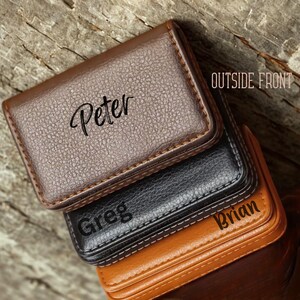 May include: A stack of three leather business card holders in brown, black, and tan. Each holder is embossed with a name: Peter, Greg, and Brian. The top holder is brown with a stitched border.