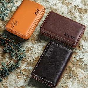 May include: Three personalized leather cardholders in shades of brown and tan are displayed. One is tan with "Happy Father's Day" and "Jeff" printed on it. The other two are brown with "Steve" and "Jake" printed on them.