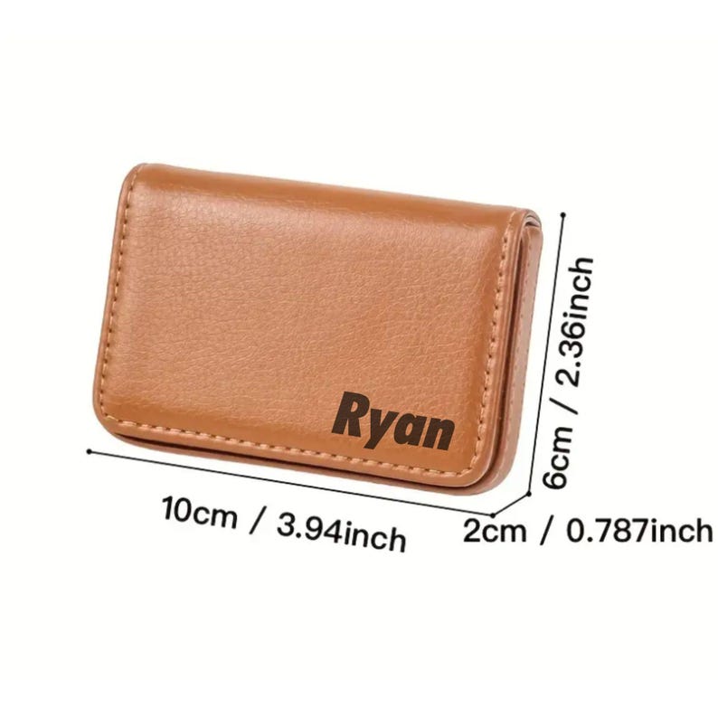 May include: A brown leather business card holder with the name "Ryan" printed on the front. The holder measures 3.94 inches long, 2.36 inches wide, and 0.787 inches thick. The card holder is rectangular with rounded corners.