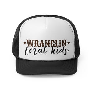 May include: A white and black trucker hat with a brown and black text design that says "WRANGLIN' feral kids" with a star on either side of the word "WRANGLIN'".