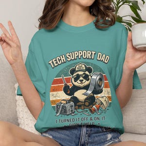 Może przedstawiać: Turkusowa koszulka z grafiką pandy w okularach przeciwsłonecznych i kapeluszu, trzymającej taśmę i śrubokręt. Tekst brzmi "TECH SUPPORT DAD" i "I TURNED IT OFF & ON. IT DIDN'T HELP."