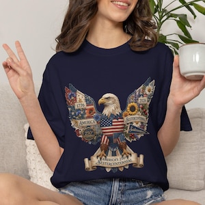 Könnte beinhalten: Marineblaues T-Shirt mit einem patriotischen Adler-Design. Die Adlerflügel sind mit Elementen der amerikanischen Flagge, Sonnenblumen und dem Text "America's 250th Sestercentennial" verziert. Das Design enthält die Jahre 1776 und 2026.