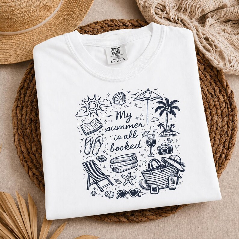 May include: A white t-shirt featuring a black ink graphic design with the text My summer is all booked. The illustration includes a sun, seashell, umbrella, palm tree, open book, flip-flops, stack of books, cocktail, camera, beach bag, and sunglasses.